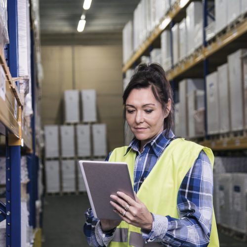 Woman holding digital tablet and putting in data in a big warehouse.